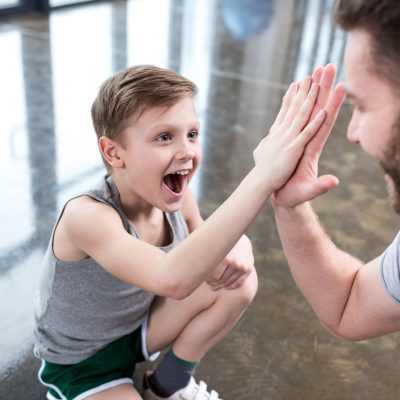 Boy giving high five to his adult friend at fitness center