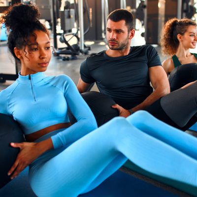 Slim women african american and caucasian ethnicity and muscular man in sportswear doing exercises with a heavy medicine ball on a rubber mat in a gym club. The concept of sports and recreation.